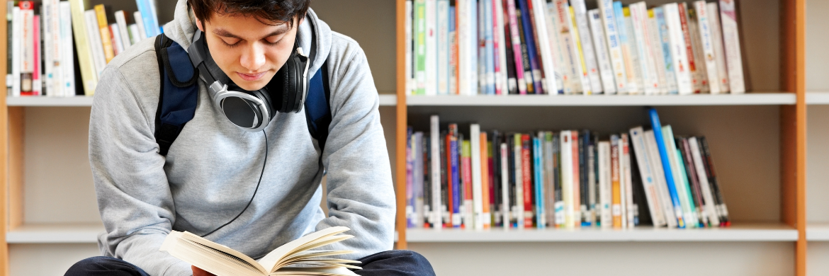 teenager sitting on the floor reading a book in a library