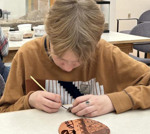 an older elementary student painting a pat sherd