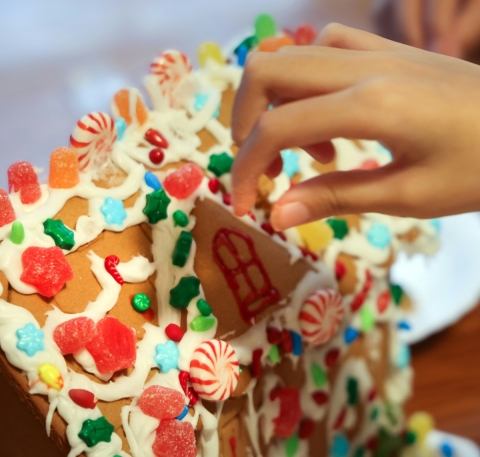 a child's hand adding candy to the room of a gingerbread house