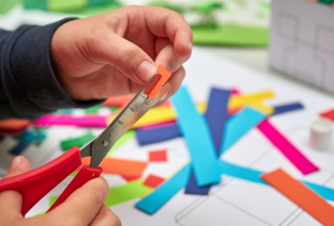 A child's hand cutting colored strips of paper. 