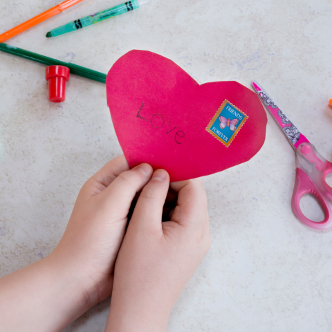 Image of a child's hands holding a red heard with the words "Love" and a stamp that says "Friends Forever"
