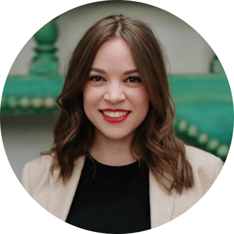 Lauren Tresp Headshot - Smiling person with light skin and wavy brown hair wearing a black shirt and beige jacket.