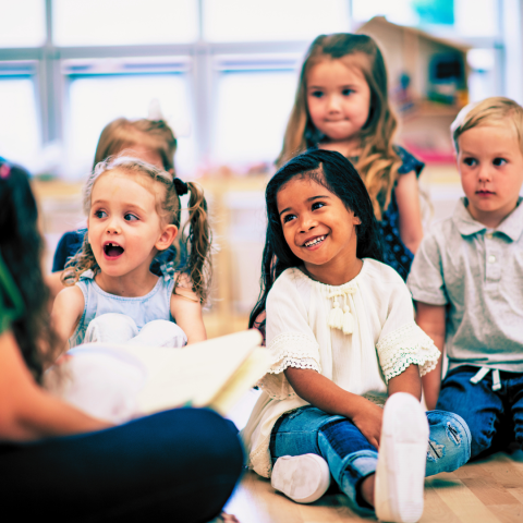 A group of smiling children sitting on the floor listening to a story.