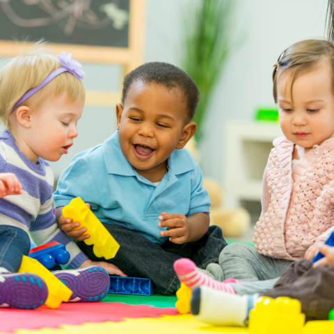 A group of toddlers sitting on a colorful mat and playing with toys.