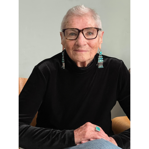 Margaret Randall headshot - A person wearing glasses and turquoise jewelry sits in a chair and looks at the camera.
