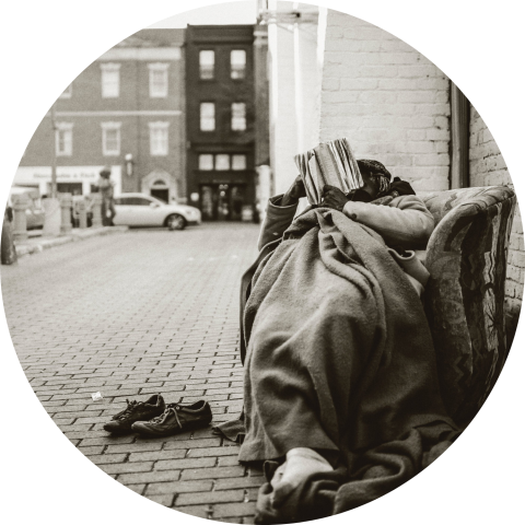 A sepia-toned photo shows a figure wrapped in blankets on a city street.