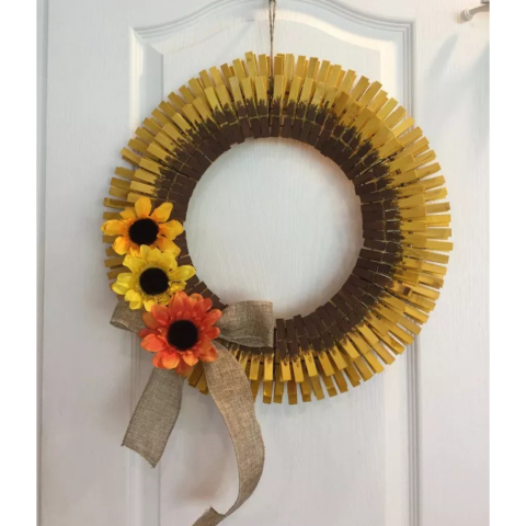 A wreath made of brown and yellow clothespins, decorated with sunflowers and a burlap bow.