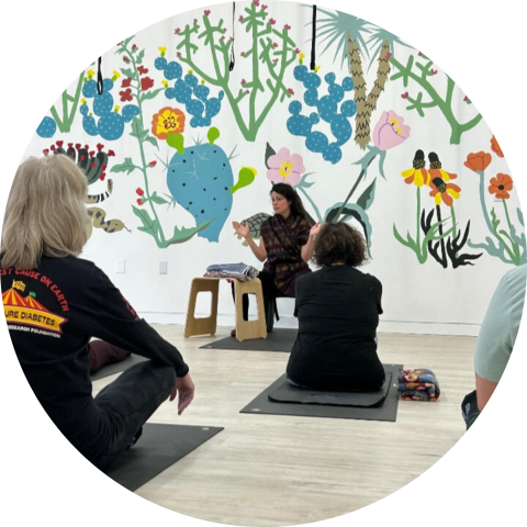 A group of people sitting on yoga listening to an instructor.