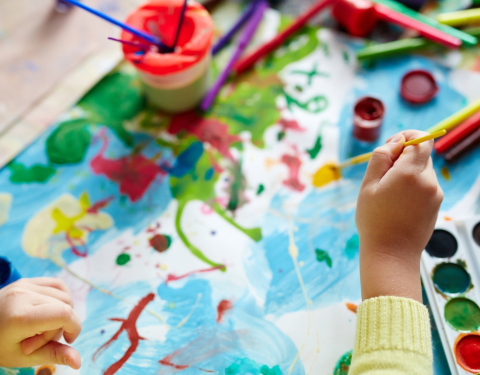 A child's hands pictured from above as they use colorful paints