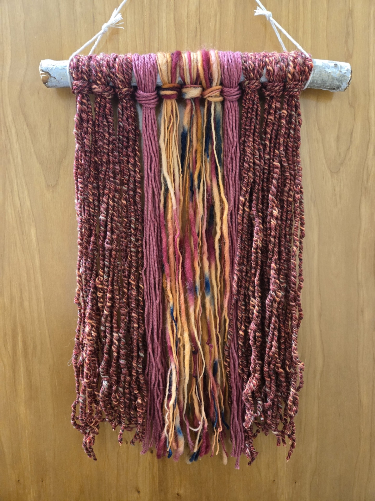 Image of a colorful wallhanging made with yarn and a branch.