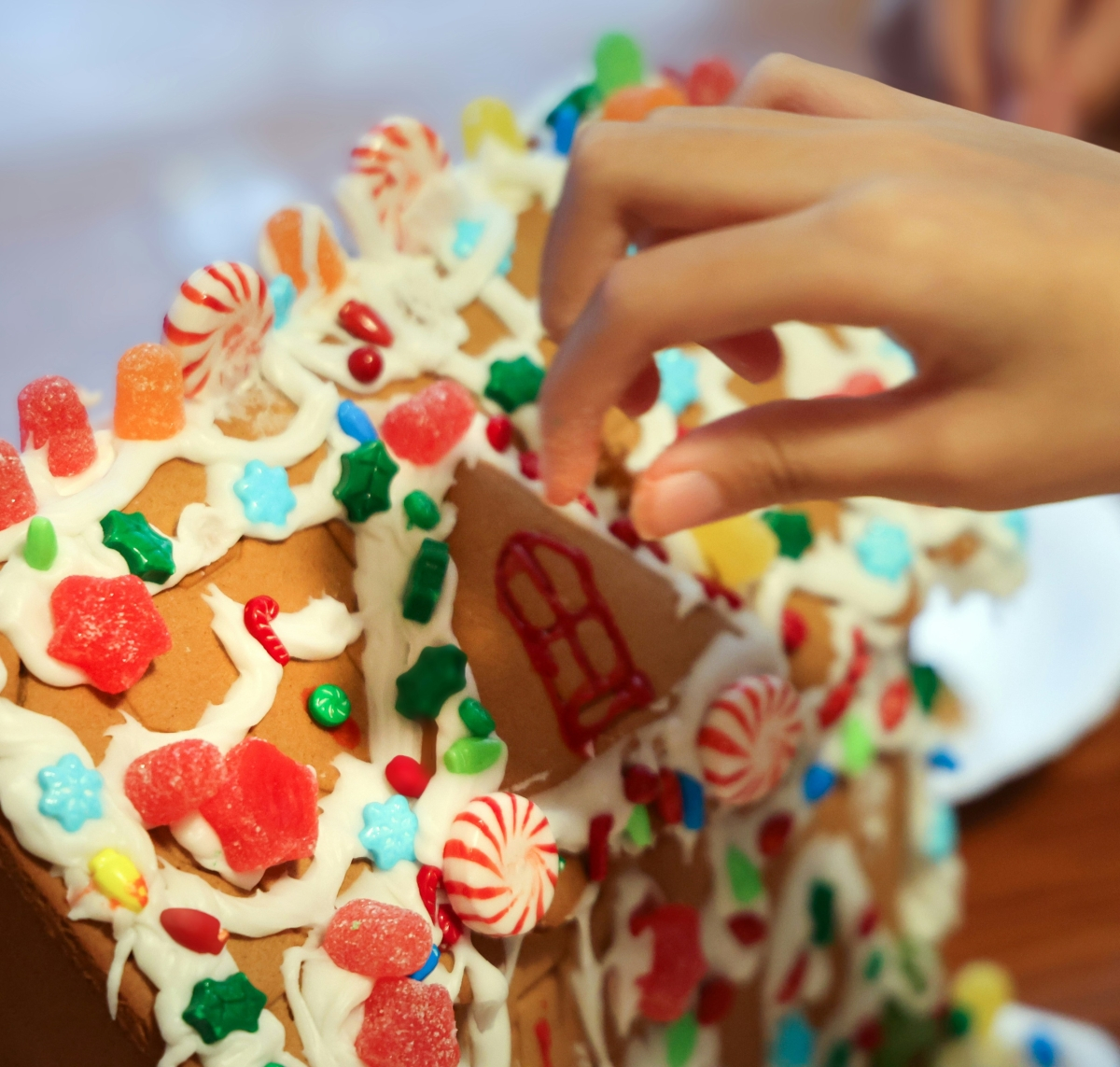 image of a child's hand adding candy to a gingerbread house