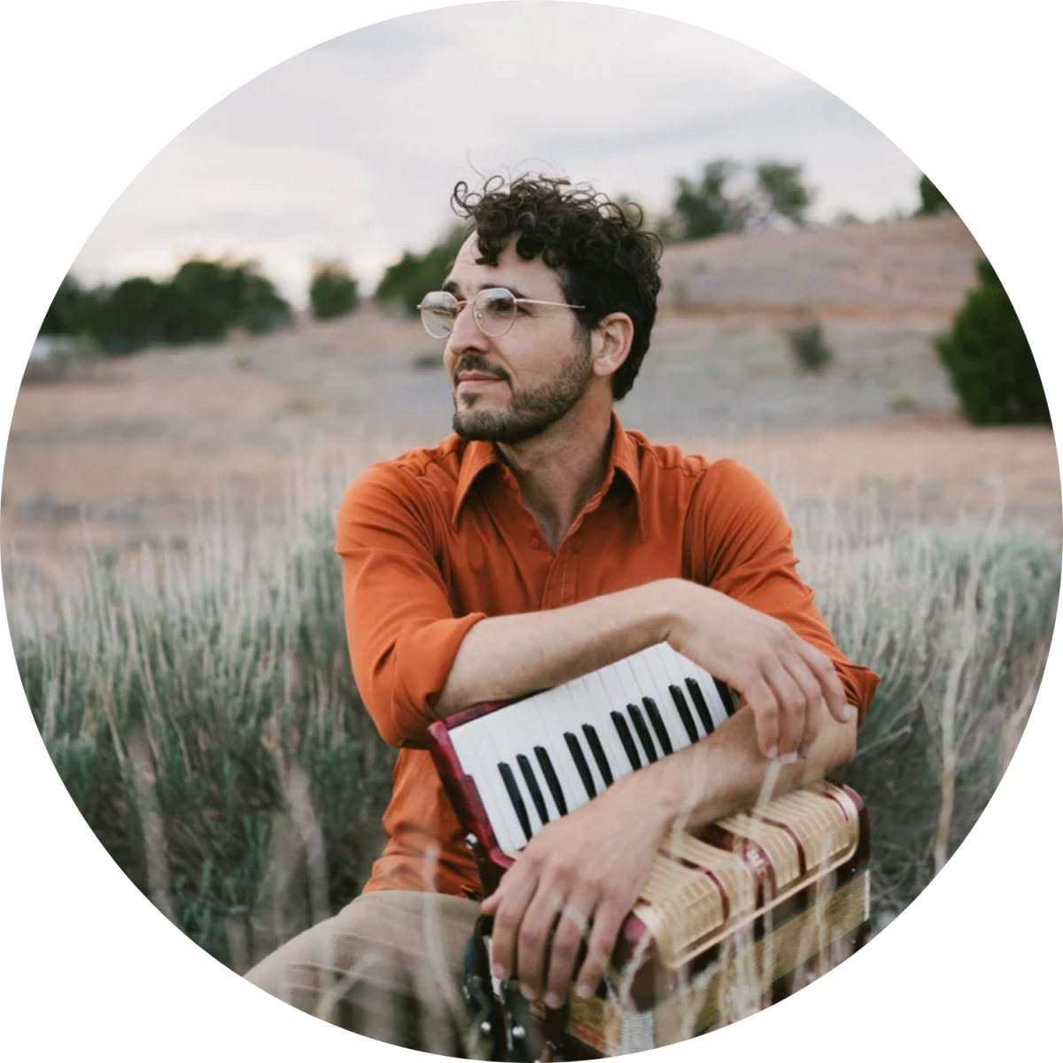A person in an orange shirt sitting outside holding a rectangular instrument.
