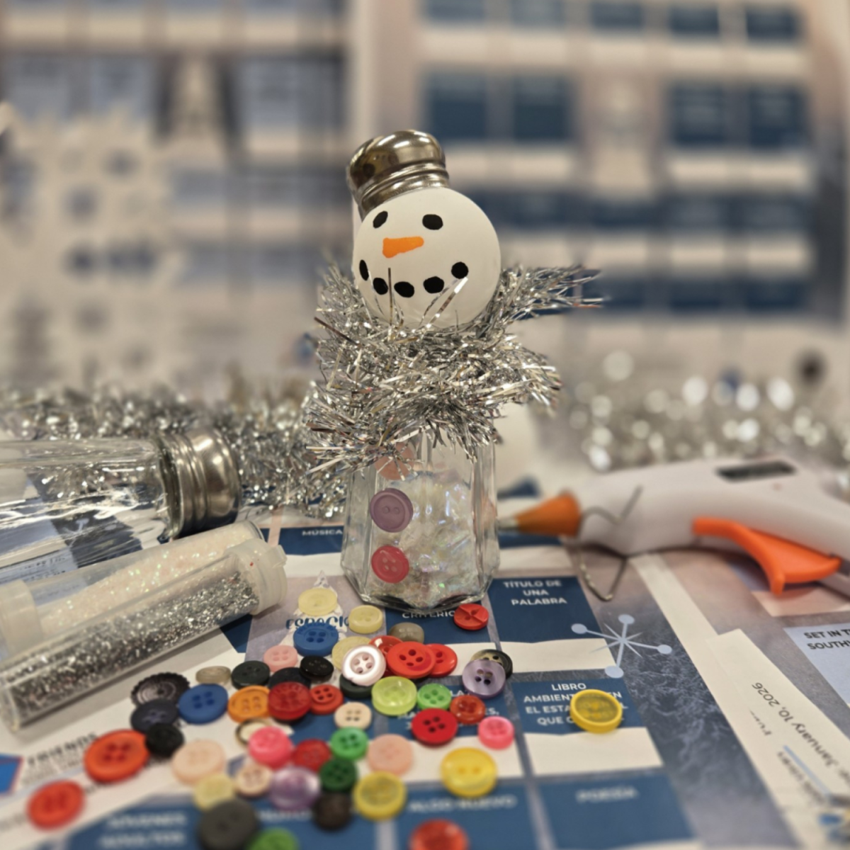 Snowman made out of a salt shaker, a table tennis ball, buttons, and tinsel.
