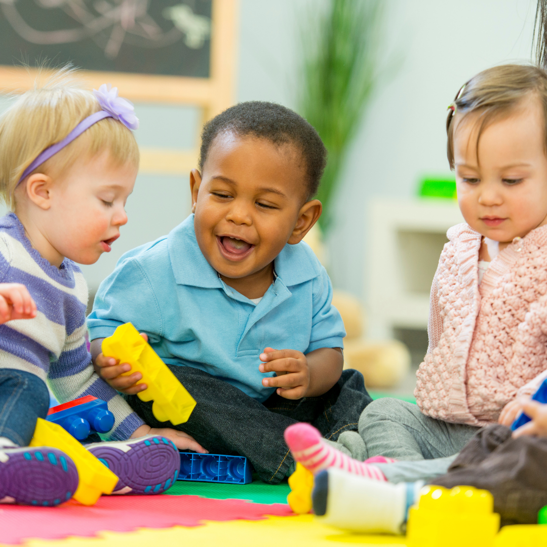 A group of toddlers sitting on a colorful mat and playing with toys.