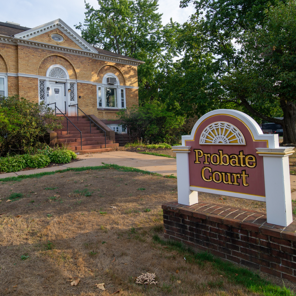 A yellow brick building with arched windows and a sign that reads "Probate Court" in front of it.