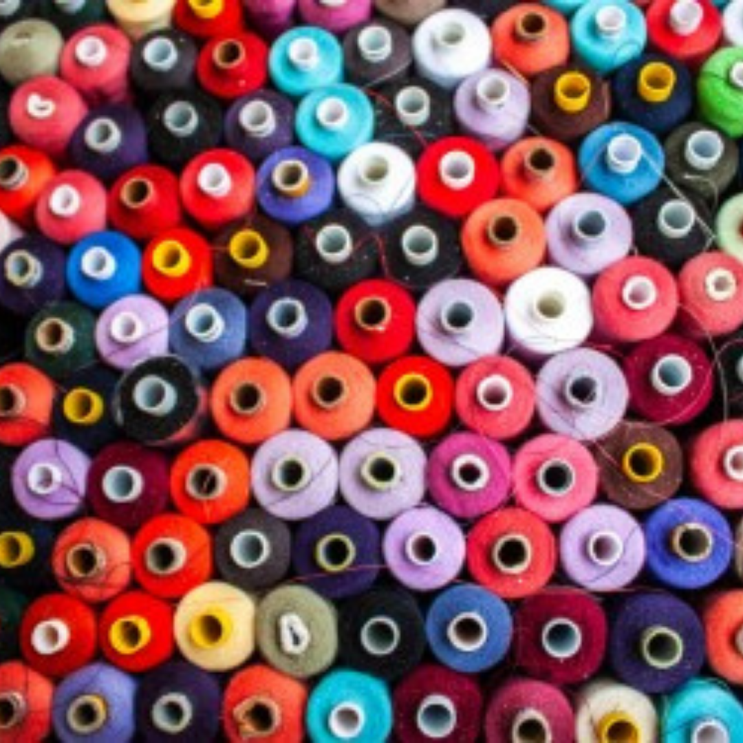 A close-up overhead view of many colorful spools of thread arranged in rows.