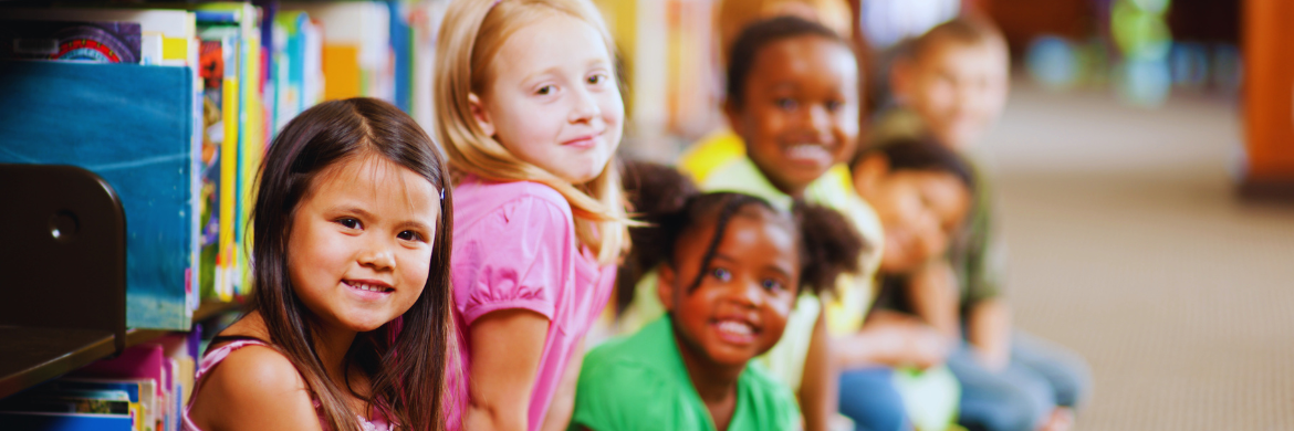 A group of smiling kids sitting in front of a library shelf.